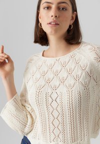 Maglione lavorato a maglia in crema, con un motivo in pizzo testurizzato a forma di diamante, maniche ampie e scollatura a girocollo.