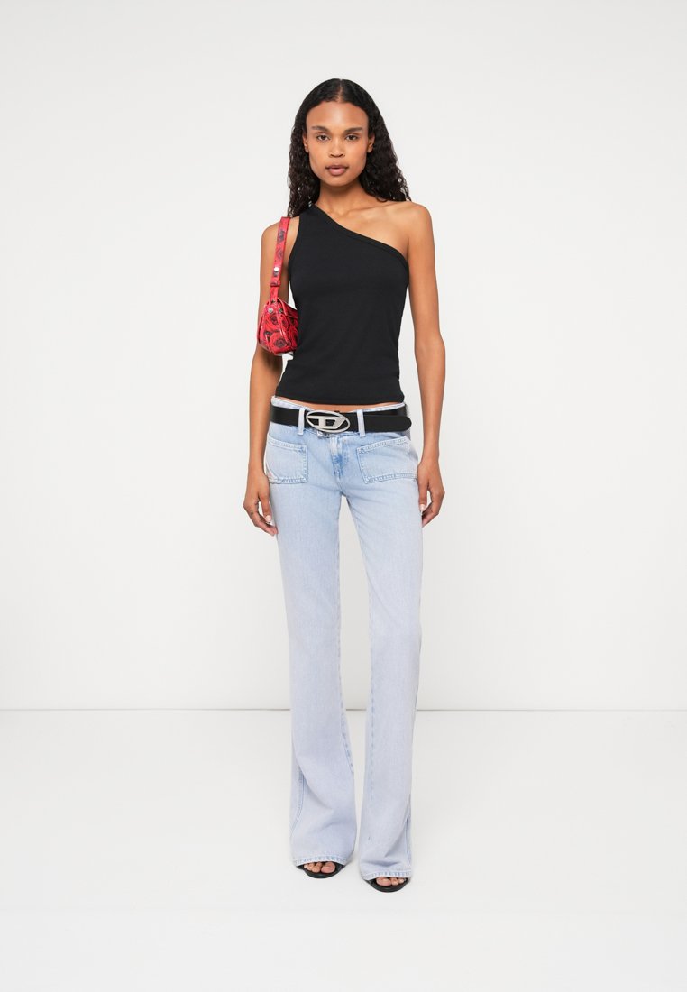 Top noir à une épaule associé à un jean évasé bleu clair. Les accessoires comprennent un sac à motifs rouges et une ceinture en argent avec une boucle distinctive.