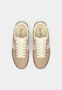 Μπεζ vegan αθλητικά παπούτσια με λευκές λεπτομέρειες, διαθέτοντας υφή στην επάνω επιφάνεια, στρογγυλεμένο μπροστινό μέρος, επίπεδα κορδόνια και καουτσούκ σόλα για πρόσφυση.