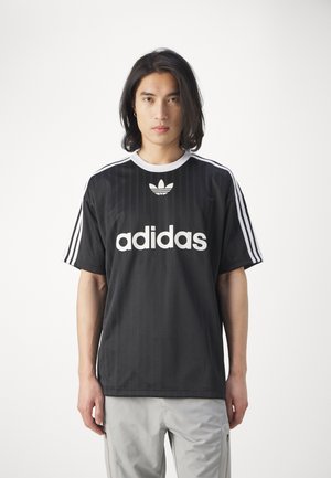 Fekete Adidas póló fehér logóval és három csíkkal a vállakon. Rövid ujjú, kerek nyakú, és függőleges bordázott textúrájú.