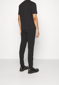 Svart bomullströja, avslappnad passform, i kombination med matchande svarta sweatpants. Svarta läderskor med texturerade sulor.