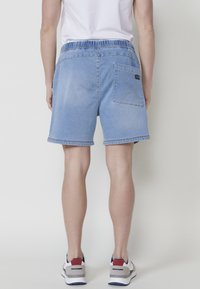 Sinised teksased šortsid, millel on elastne vöökoht ja tagaTasku, omavad pleekinud pesu ja kontrastset õmblust. Lühike pikkus ja servad on lõpetatud.