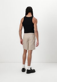 Sort tanktop, beige cargoshorts med sidelommer og sorte sko. Modelen vender væk fra kameraet og fremviser outfitets pasform og farvekombination.