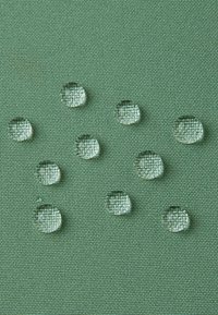 Gocce d'acqua trasparenti su un tessuto verde testurizzato, che mette in mostra un motivo intrecciato. Le gocce variano in dimensione e sembrano sparse.