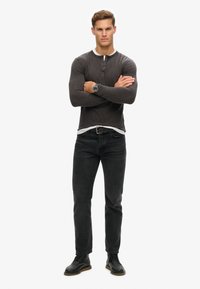 Donkergrijze langemouwen henley shirt met knopen, gelaagd over een wit shirt. Gepaard met zwarte jeans en zwarte veterschoenen.