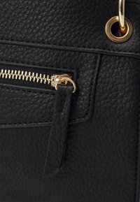 Borsa a mano in pelle nera testurizzata con cerniera dorata, un piccolo cartellino e un occhiello in metallo. Il design è rettangolare con cuciture visibili.