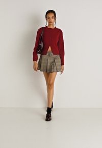 Κόκκινο, πουλόβερ με κουμπάκια, μακρύ μανίκι και κοντή σχεδίαση, συνδυασμένο με καρό σορτς ψηλής μέσης με πιέτες. Τα αξεσουάρ περιλαμβάνουν μια τσάντα.