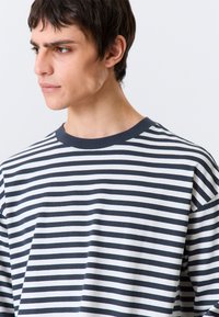 Ριγέ μπλούζα μακριάς μανίκιας σε ναυτικό μπλε και λευκό. Κατασκευασμένη από βαμβάκι, διαθέτει στρογγυλή λαιμόκοψη, άνετη γραμμή και ομοιόμορφες ορι ζόντιες ρίγες.