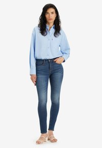 Camisa celeste de botones con mangas largas, combinada con pantalones ajustados azul oscuro y sandalias blancas de tacón. Ajuste casual.