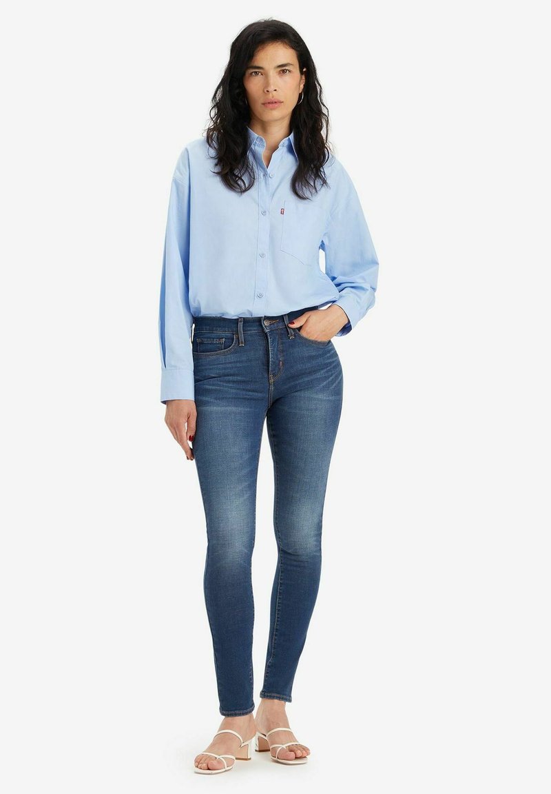 Camisa celeste de botones con mangas largas, combinada con pantalones ajustados azul oscuro y sandalias blancas de tacón. Ajuste casual.