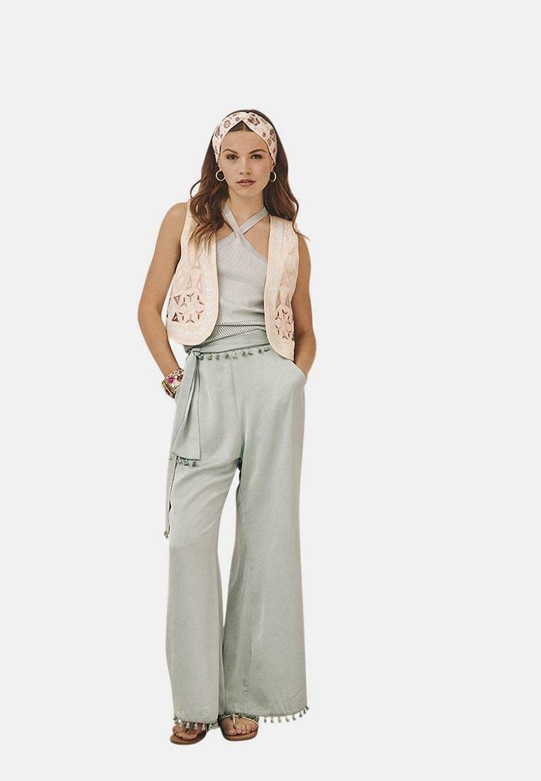 Chaleco sin mangas ligeramente estampado sobre una camiseta gris, combinado con pantalones de pierna ancha en color verde menta con detalles de pompones en el dobladillo.