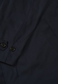 Tumesinine jakk, millel on sile tekstuur, kaks musta nuppu ja küljetasku. Lihtne disain ilma nähtavate mustrite või aksessuaarideta.