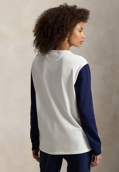 T-shirt à manches longues avec un corps blanc et des manches bleu marine, présentant une texture côtelée et un col rond. Coupe lisse et décontractée.