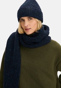 Granatowy zestaw czapki z dzianiny i szalika o prążkowanej fakturze, zestawiony z oliwkowozielonym swetrem. Miękkie, ciepłe materiały o przytulnym designie.