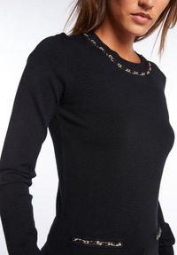 Pullover nero a maniche lunghe con collo rotondo, caratterizzato da una catena dorata intorno al collo e dettagli dorati sulle tasche.