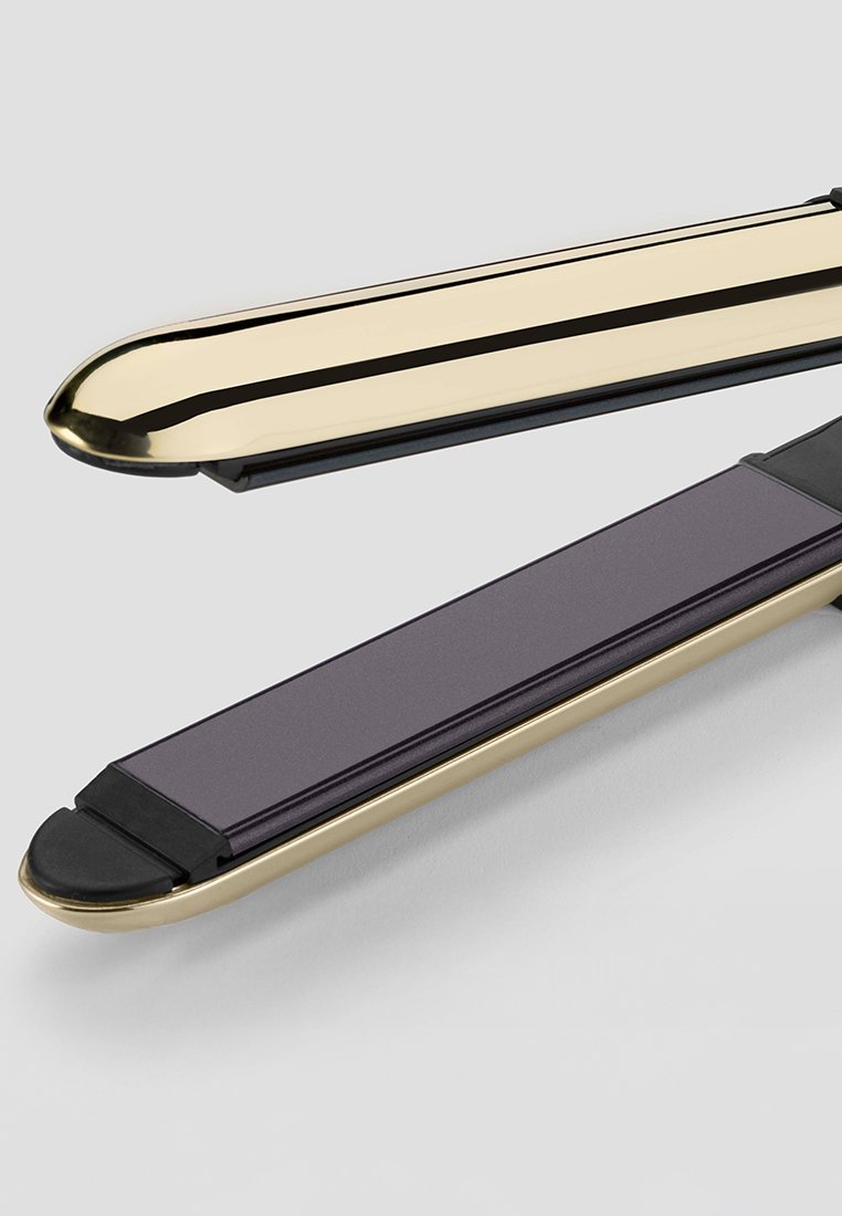 Prostownica do włosów w złotym i czarnym metalicznym wykończeniu, charakteryzująca się eleganckim designem i gładkimi, ciemnymi ceramicznymi płytkami zapewniającymi równomierne stylizowanie.