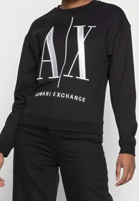 Sudadera negra con gráfico blanco "AX" y texto "Armani Exchange". Cuenta con mangas largas y un dobladillo acanalado. Textura de tela suave.