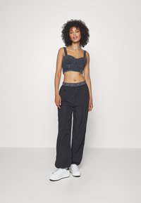 Farmer szövet crop top széles pántokkal, fekete, magas derekú nadrággal és fehér tornacipővel. Jellemzője a logóval ellátott derékpánt és a texturált anyag.