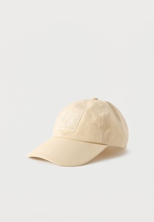 Beež puuvillane pesapallimüts kõverdatud visiriga ja valge ristkülikukujuline plaastriga, millel on ees kiri "MAISON KITSUNÉ".