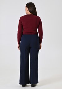 Maglione bordeaux con aperture sulle spalle abbinato a pantaloni a gamba larga blu navy con vita alta. Texture liscia e vestibilità rilassata. Stivali neri alla caviglia.