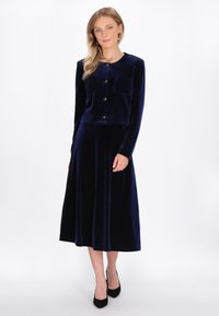 Navy velours twee-delig set met een cropped, lang mouwen jasje met gouden knopen en een bijpassende lange rok, beide met een gladde textuur.