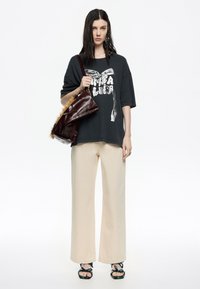 Camiseta negra de gran tamaño con estampado gráfico; pantalones anchos beige; bolso burdeos brillante con un acento de piel; sandalias verdes con tiras.