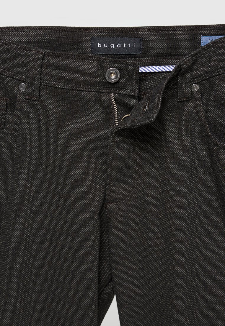 Dunkel strukturierte Hose mit offenem Reißverschluss und Knopf, die das Bugatti-Label am Bund und ein gestreiftes Stoffdetail innen zeigt.