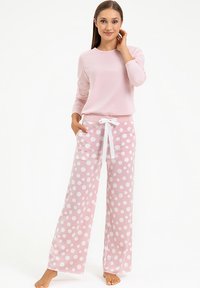 Różowa bluzka z długim rękawem zestawiona z szerokimi spodniami piżamowymi w kropki, które mają białe kropki i biały sznurek do wiązania. Miękki materiał.