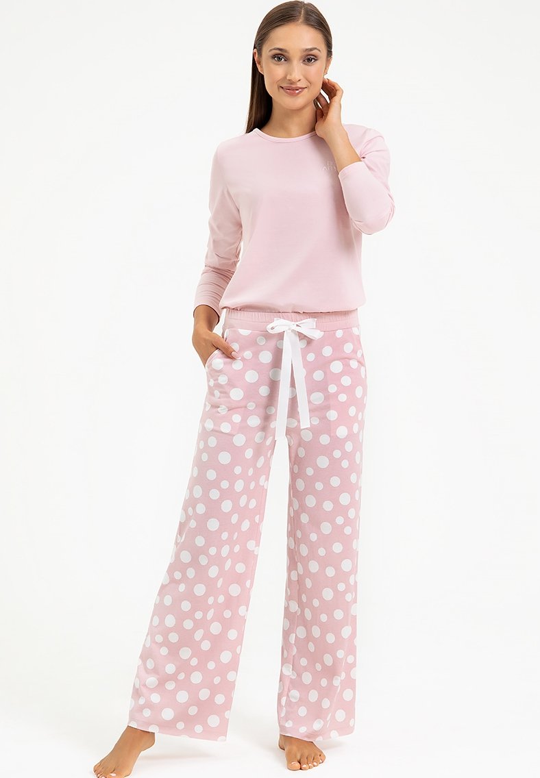 Różowa bluzka z długim rękawem zestawiona z szerokimi spodniami piżamowymi w kropki, które mają białe kropki i biały sznurek do wiązania. Miękki materiał.