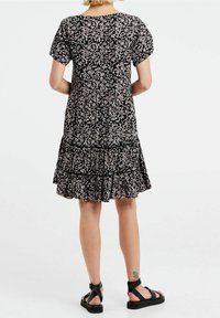 Musta kukallinen mekko, jossa on lyhyet hihat, kerroksellinen röyhelöhelma ja pyöreä pääntie. Valmistettu kevyestä kankaasta, joka on pehmeä tekstuuriltaan.