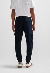 Marinblå jogger-byxor med sidofickor, elastiska muddarna och en smidig textur, kombinerade med en vit t-shirt och vanliga sneakers.