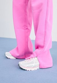 Różowe spodnie dresowe o luźnym kroju, zestawione z jasnoszarymi i białymi butami sportowymi z siateczkowymi wstawkami i różowymi akcentami.