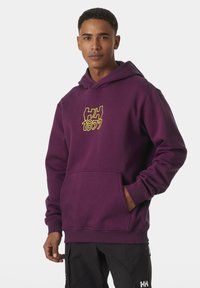 Sudadera morada con un bolsillo frontal y capucha ajustable con cordón, que presenta un logo gráfico amarillo "HH 1877" en el pecho. Textura suave.