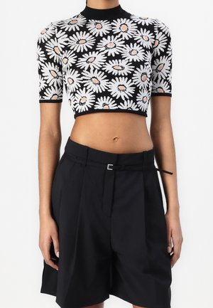 Černý crop top s bílými a broskvovými sedmikráskovými vzory v kombinaci s černými high-waisted šortkami na míru s tenkým páskem.