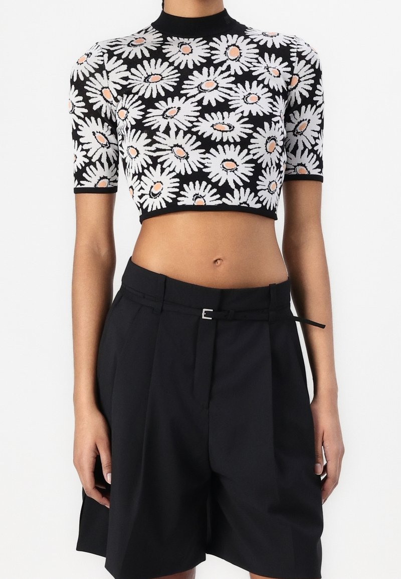 Top court noir avec motif marguerite blanc et pêche, associé à un short noir taille haute et ajusté avec une fine ceinture.
