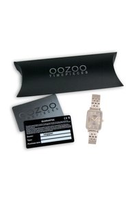 Montre rectangulaire OOZOO avec un bracelet en métal argenté et un cadran gris, arborant des marqueurs horaires en or. Comprend une carte de garantie noire et une boîte.