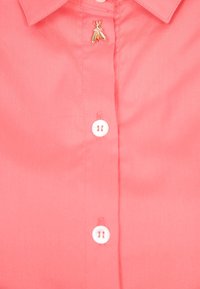Camisa de botón color coral hecha de tela, con botones blancos y un pin decorativo de insecto dorado cerca del cuello. Textura suave.