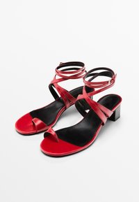 Des sandales à talons blocs en cuir rouge présentent des sangles entrecroisées et un design à bout ouvert, avec une semelle intérieure noire contrastante pour un détail supplémentaire.