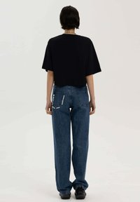 Korte mouwen zwart T-shirt in cropped stijl, gecombineerd met losse blauwe jeans met textiellabels en een relaxte pasvorm. Schoenen zijn zwarte sneakers.
