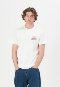 Hvit bomull t-skjorte med korte ermer, med en flerfarget solgrafikk og teksten "RIP CURL" på venstre bryst. Avslappet passform.