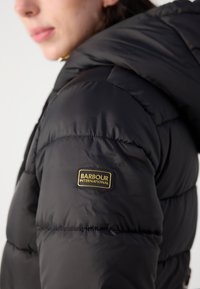 Zwarte pufferjas met een geborduurd patroon. Voorzien van een capuchon en een gouden "Barbour International" logo-patch op de linker mouw.