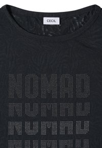 Chemise noire à encolure ronde, étiquette de marque "CECIL" et le mot "NOMAD" répété en motif à pois sur le devant.