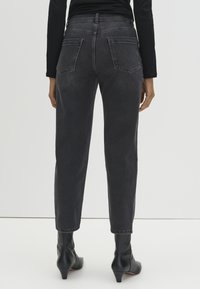 Person wearing black washed straight-leg jeans, black long-sleeve top, and black heeled ankle boots, standing against a plain background.