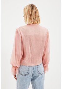 Rosa stickad cardigans med genomskinlig puffärmsdesign, har en strukturerad baksida och ribbad nederkant. Matchad med ljusa denimjeans.