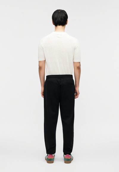 Μαύρο παντελόνι φόρμας με ελαστική μέση, συνδυασμένο με ανοιχτογκρι κοντομάνικο μπλουζάκι, από πίσω όψη.