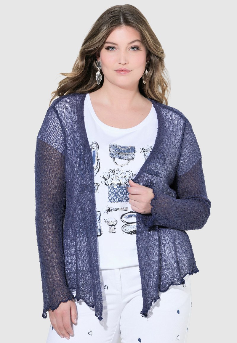 Mörkblå, lättvikts, öppna cardigan med lång ärm och vågformad fåll. Texturerat stickat material, lager på lager över en vit grafisk t-shirt.