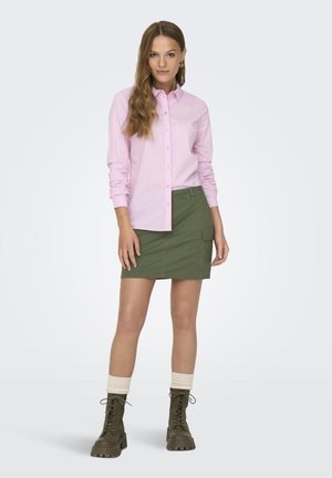 Light pink, vertically striped button-up shirt paired with a khaki green mini skirt. Brown lace-up boots with cream-toned cuffs.