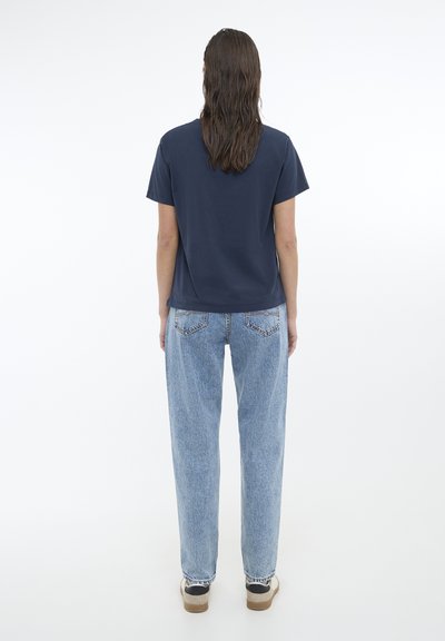 Tricou de culoare navy cu mânecă scurtă, asortat cu blugi deschiși, cu talie înaltă. Blugii au o textură uzată și sunt ușor supradimensionați.
