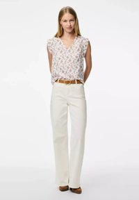 Blusa a stampa floreale con maniche corte e scollatura a V; abbinata a pantaloni a campana bianchi sporchi e cintura marrone. Modella in piedi con le mani dietro.