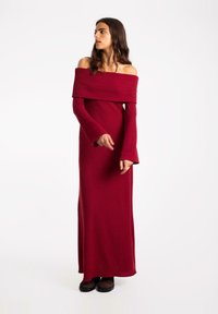 Robe longue rouge décolletée, confectionnée dans un tissu doux, avec de longues manches à poignets évasés et une silhouette ajustée.
